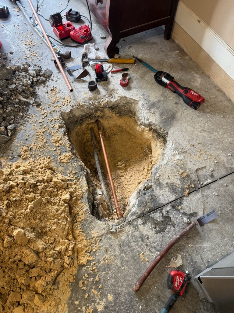 Replacement copper pipe in an opened concrete floor, with a press tool and repair supplies nearby.